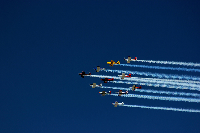 Planes streak across a deep blue sky trailing lines of white smoke.