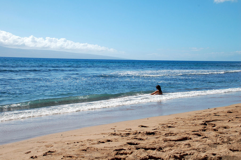 White wash runs up onto golden sand where a woman sits letting the water run over her.